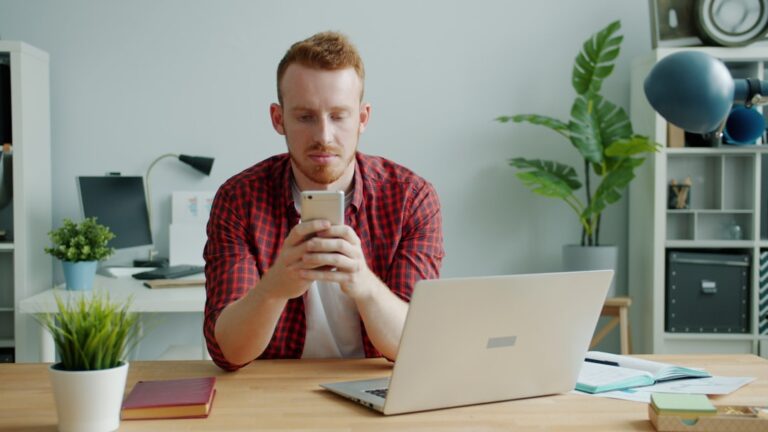 Homem Com Cabelo Vermelho Usando Smartphone Na Mesa Com Laptop R xd9TJSWeM