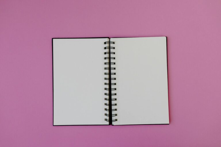 Flat lay of an open spiral notebook on a vibrant pink background, perfect for creativity.