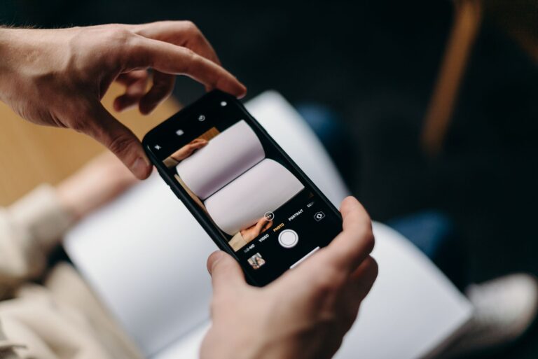 Person using smartphone to photograph blank open book. Concept of mobile photography and creativity.