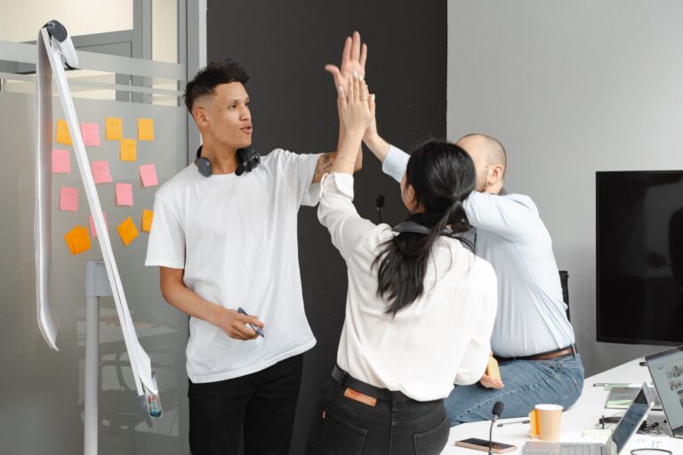 Three colleagues celebrate success with a high-five in a modern office.
