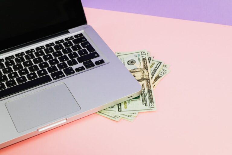 Close-up of a laptop with US dollar bills on a pastel background, symbolizing finance.