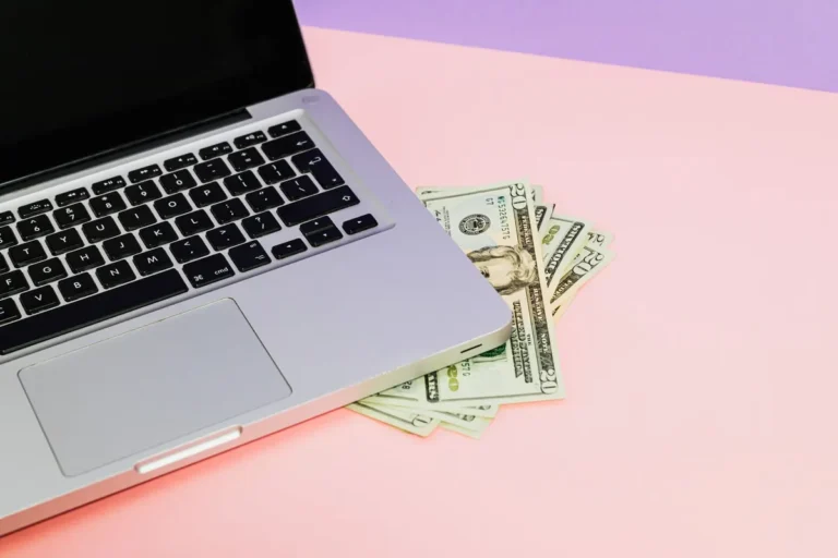 Close-up of a laptop with US dollar bills on a pastel background, symbolizing finance.