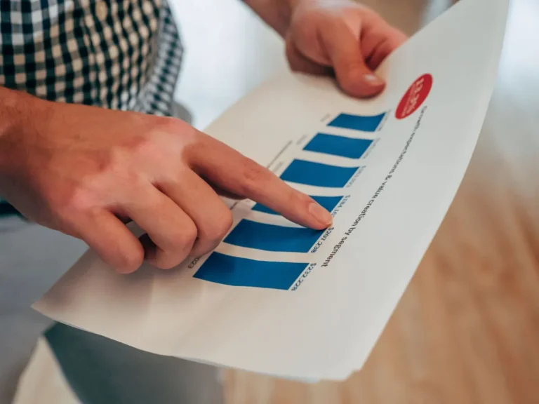 Close-up of hands pointing at a bar chart on paper, analyzing financial stats and report.