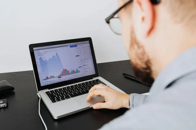 Man working on a laptop analyzing business data and financial graphs indoors.